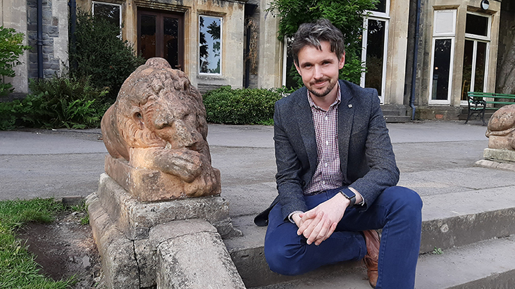 Gray Hill sitting on steps next to a statue of a lion nuzzling its paw