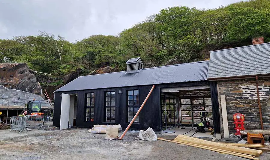 A newly built workshop with black cladding next to older stone buildings