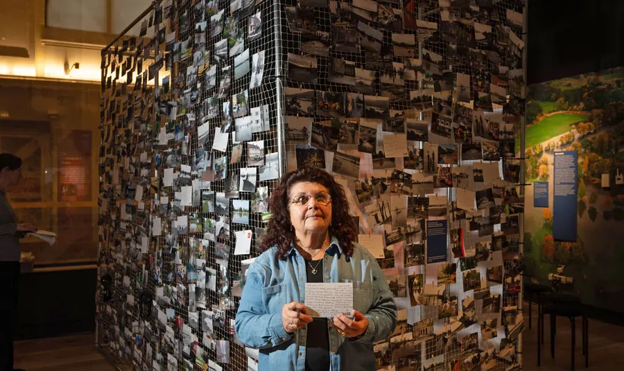 A person stands in front of a large display of photos holding a card about their experiences of local flooding