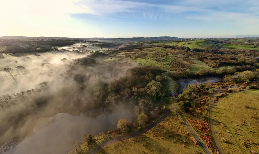 Aerial view of a green landscape in Wales, including fields, trees, water and mist rolling in