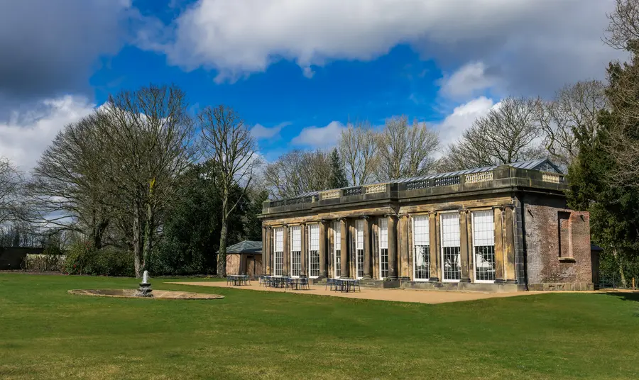 Camellia House at Wentworth Woodhouse. A Georgian stone building with glass roof and large windows. A lawn and stone fountain are in front of the building