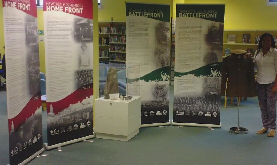 Newcastle remembers exhibition A woman stands by four pull up displays, a model uniform on a mannequin and a glass case containing replica first world war objects