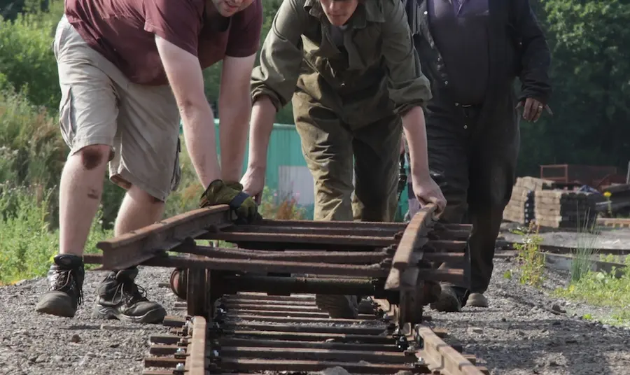 Two teenage trainees lay a new railway track by hand supervised by an older volunteer