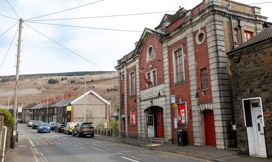 Tylorstown Welfare Hall stands out as the largest building on a street of traditional terraced houses, with the valley side in the background.