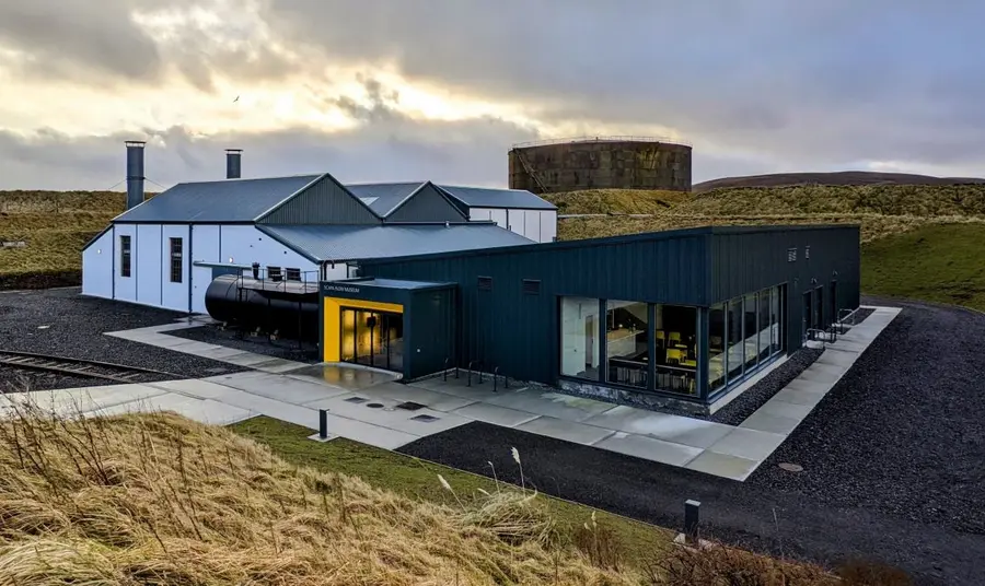 The expanded Scapa Flow Museum. The Scapa Flow Museum, with an older structure of white warehouse spaces to the left, connected to a contemporary, single-storey expansion to the right, with a new entrance and café visible.