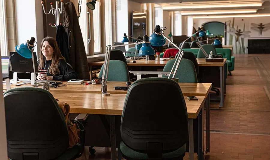 A person sitting at a desk in a coworking space with green chairs and murals of insects
