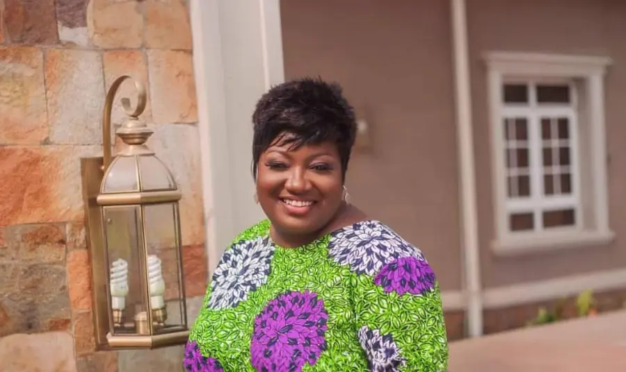 a black woman wearing a colourful dress, standing against a building