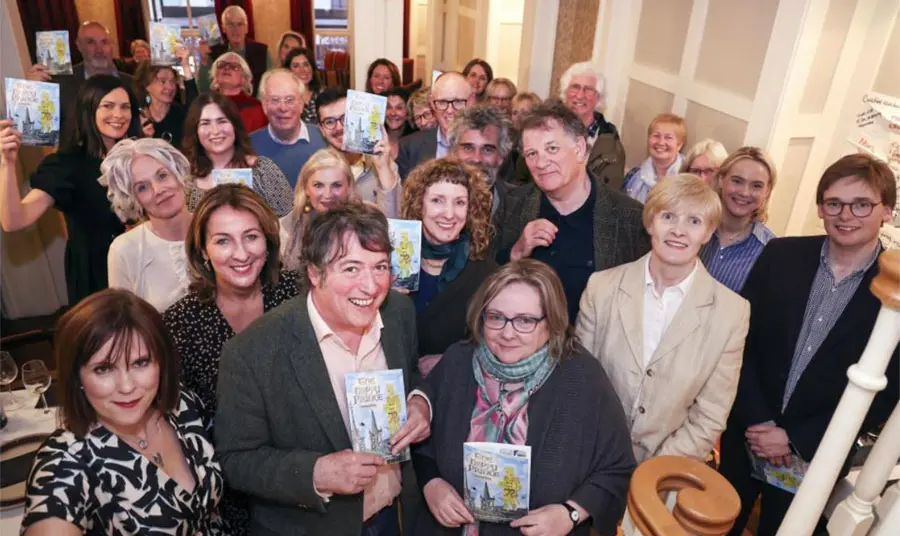 A group of people in the lobby of a building, each looking at the camera and holding up a booklet