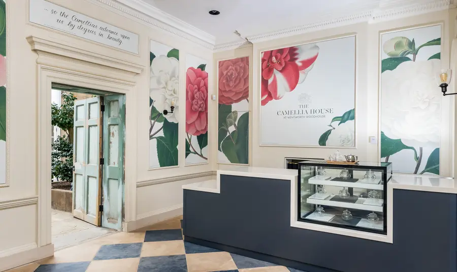 Interior of The Camellia House at Wentworth Woodhouse A cafe counter inside a room with a chequered tiled floor. Panels are on the wall behind the counter with illustrations of camellias.