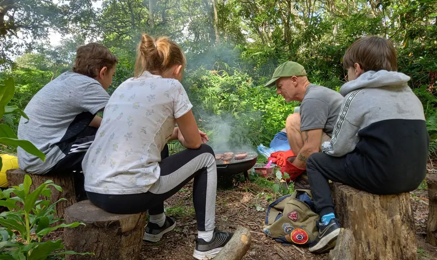Young people and an adult sit around a barbeque