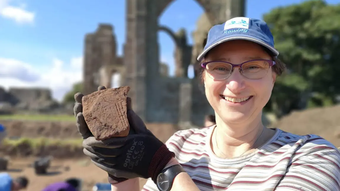 A person at an archaeological dig site holds up a piece of stone which has been excavated