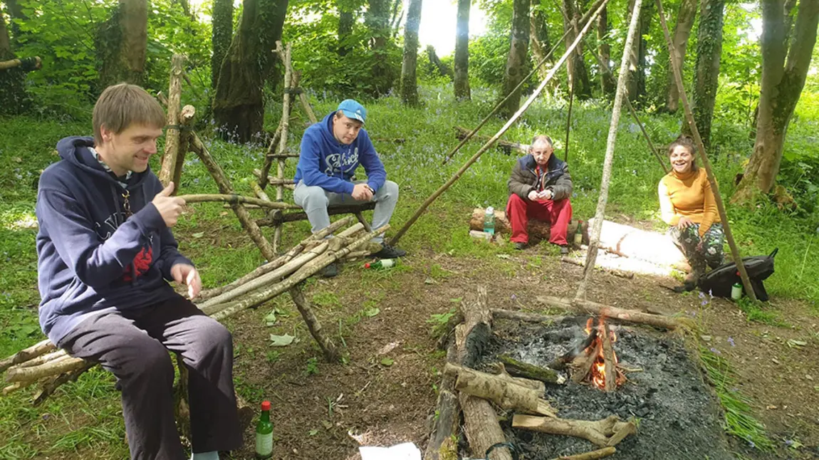 Grantiau cymunedol yn rhoi hwb i lesiant ledled Cymru People chat round a campfire in woodland
