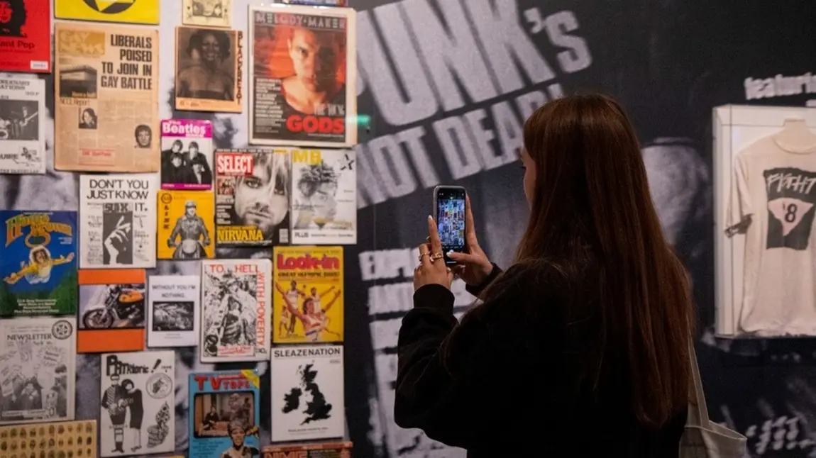 Display of gig posters at The Museum of Youth Culture Image of person with long dark hair and dark clothing taking a picture on a mobile of a display of music gig posters at The Museum of Youth Culture