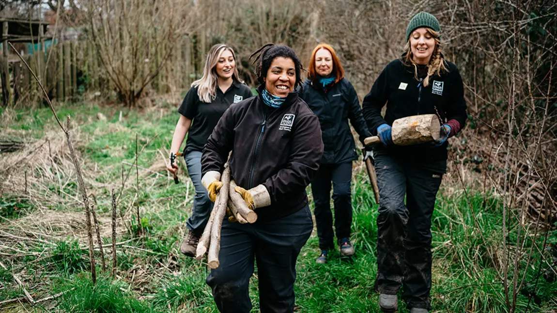 Three women carrying logs in a park