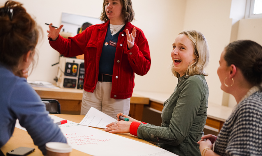Women sitting around a table looking happy as someone standing speaks to them